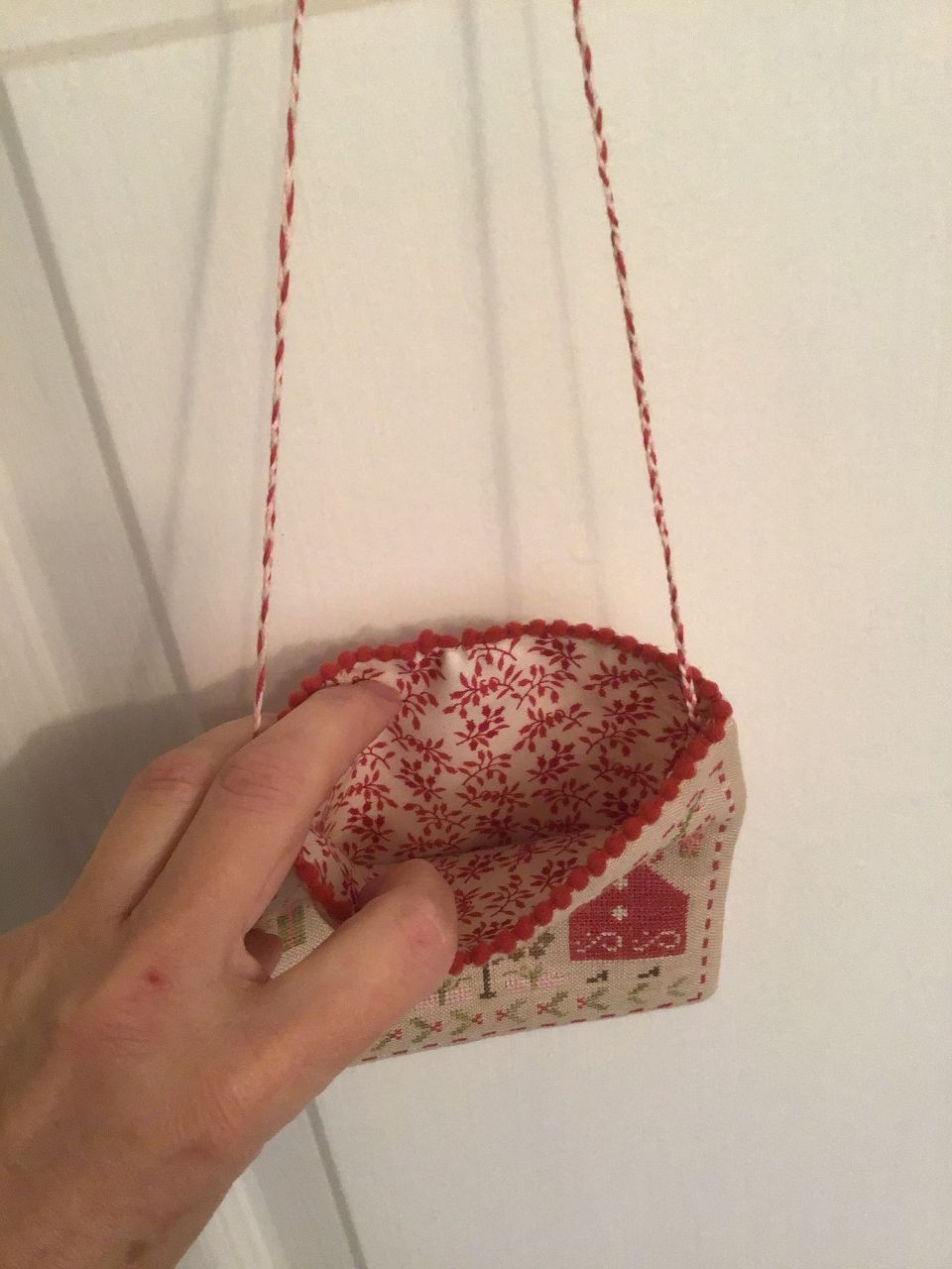 This is Merry and Bright by Pineberry Lane.  I finished the stitching earlier this year.  Assembly into a lined hanging pouch with pom pom trim and braided hanger was done yesterday and today.…..just in time for holiday decorating.  The fabric on the back of pouch is the same as inside lining fabric.