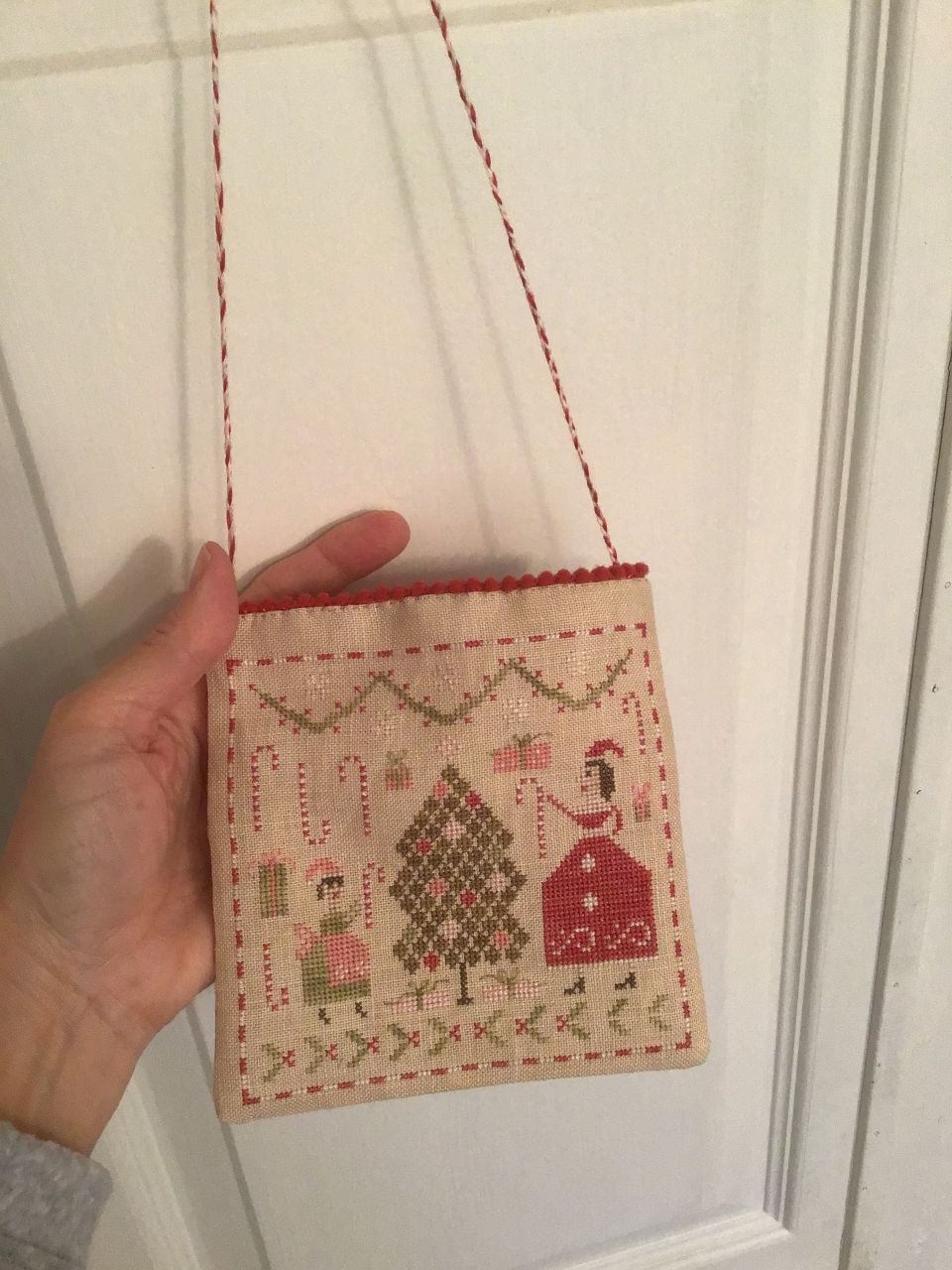 This is Merry and Bright by Pineberry Lane.  I finished the stitching earlier this year.  Assembly into a lined hanging pouch with pom pom trim and braided hanger was done yesterday and today.…..just in time for holiday decorating.  The fabric on the back of pouch is the same as inside lining fabric.